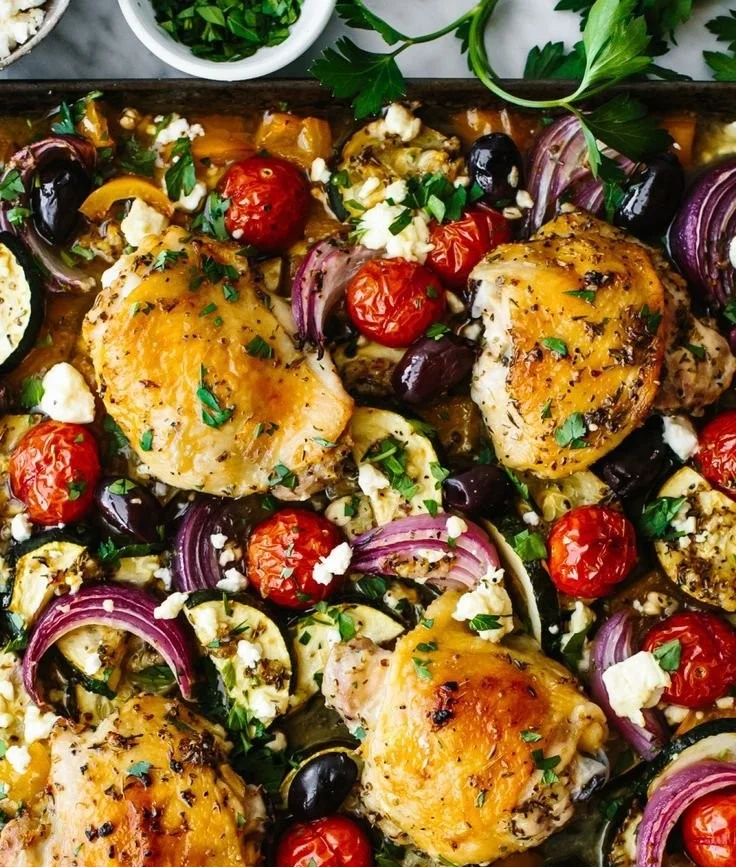 Delicious Greek sheet pan chicken garnished with vegetables on a baking tray.
