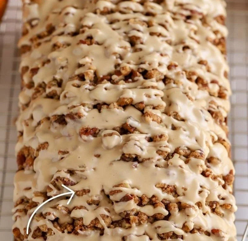 Slice of moist maple pumpkin bread on a wooden table, garnished with walnuts.