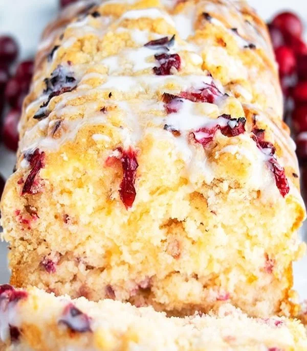 Sliced orange-glazed cranberry bread on a wooden cutting board