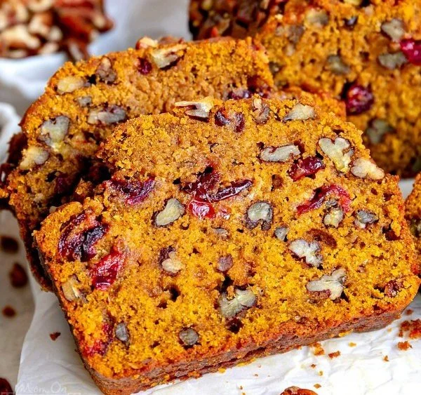 Loaf of pumpkin bread with cranberries and pecans on a wooden cutting board
