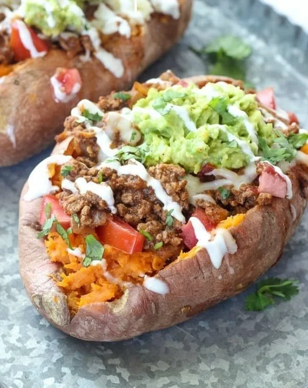 Sweet potatoes stuffed with taco filling, garnished with fresh toppings.